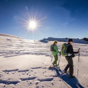 A couple holding hiking poles and walking in the snow