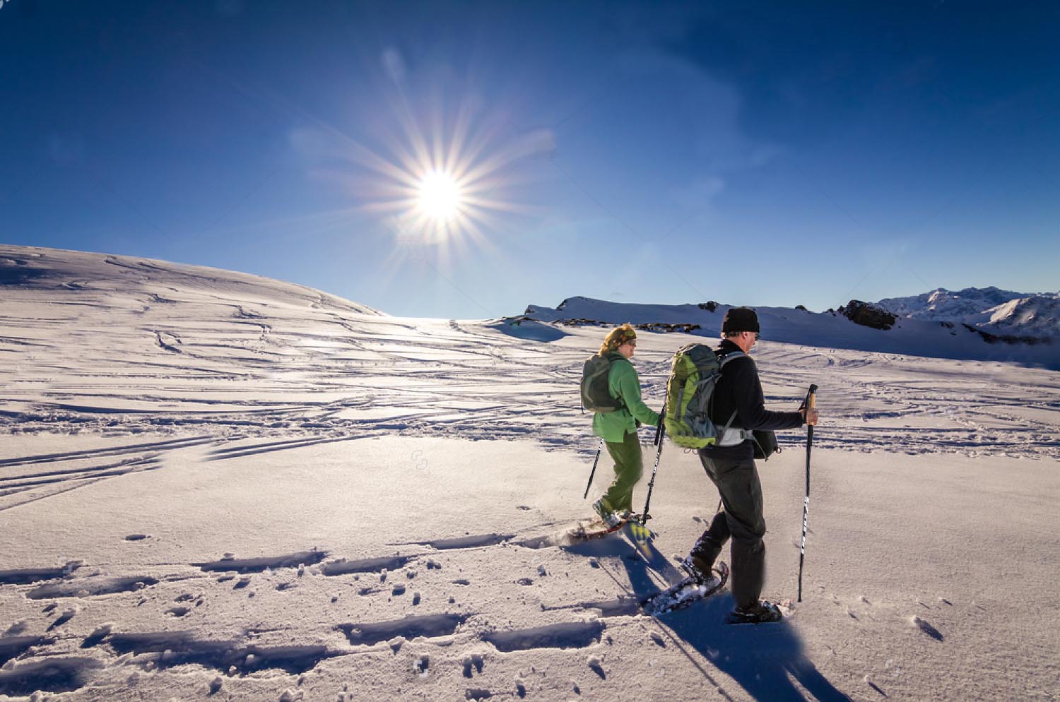 A couple holding hiking poles and walking in the snow